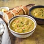 A bowl of split pea soup served with slices of crusty bread and a pat of butter on the side.