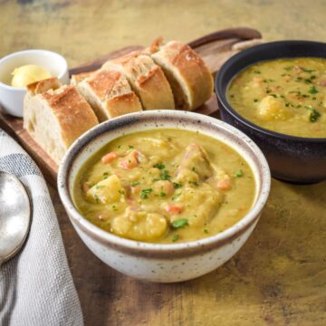 A bowl of split pea soup served with slices of crusty bread and a pat of butter on the side.