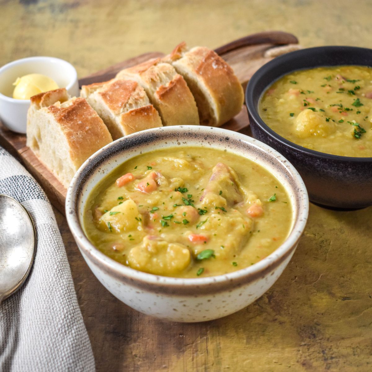 A bowl of split pea soup served with slices of crusty bread and a pat of butter on the side.