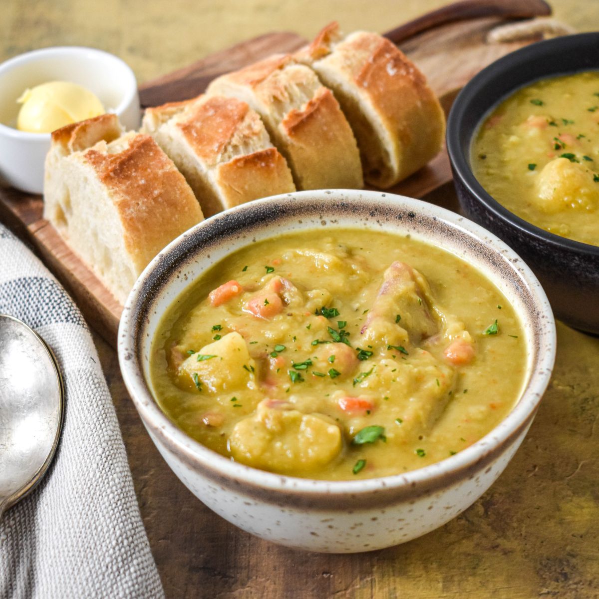 Overhead view of the soup in a white bowl with a black bowl and sliced bread in the background.