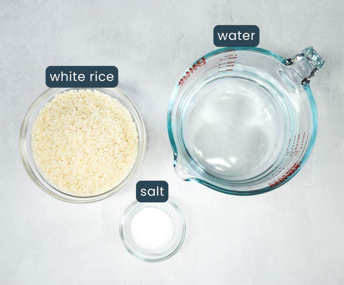 Ingredients for white rice: bowl of uncooked rice, measuring cup of water, and small bowl of salt, clearly labeled.