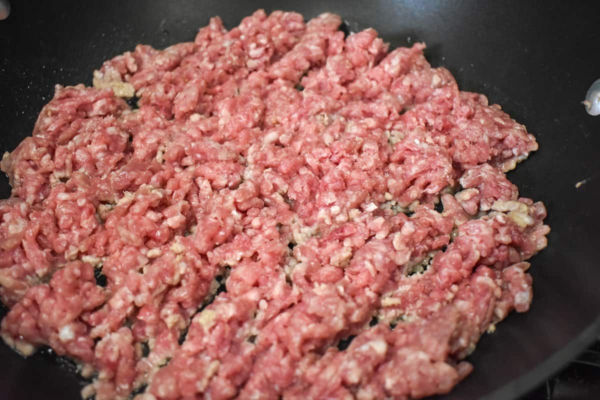 Ground pork that hasn't browned yet in a large, black skillet.