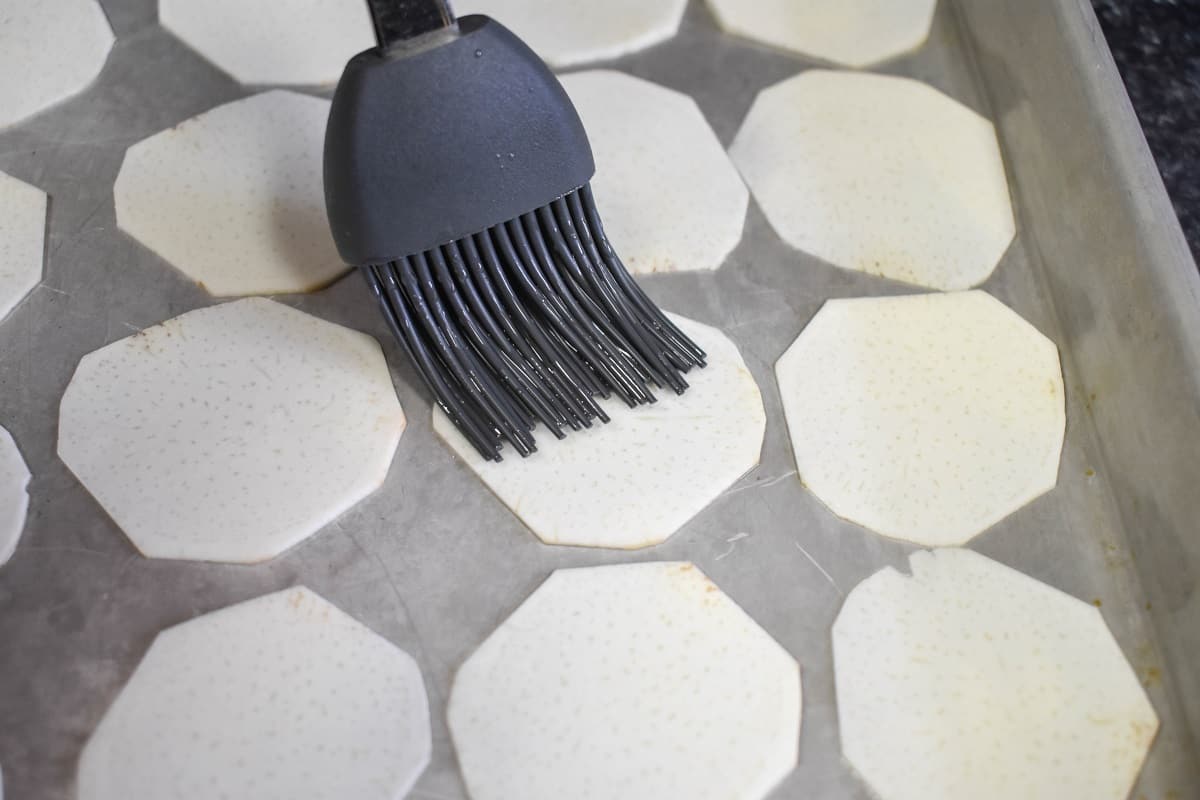 A gray, silicone pastry brush, brushing oil on a malanga round.