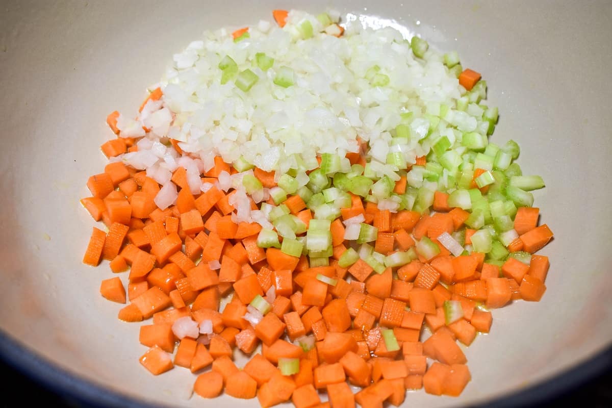 Diced onions, carrots and celery cooking in a white pan.