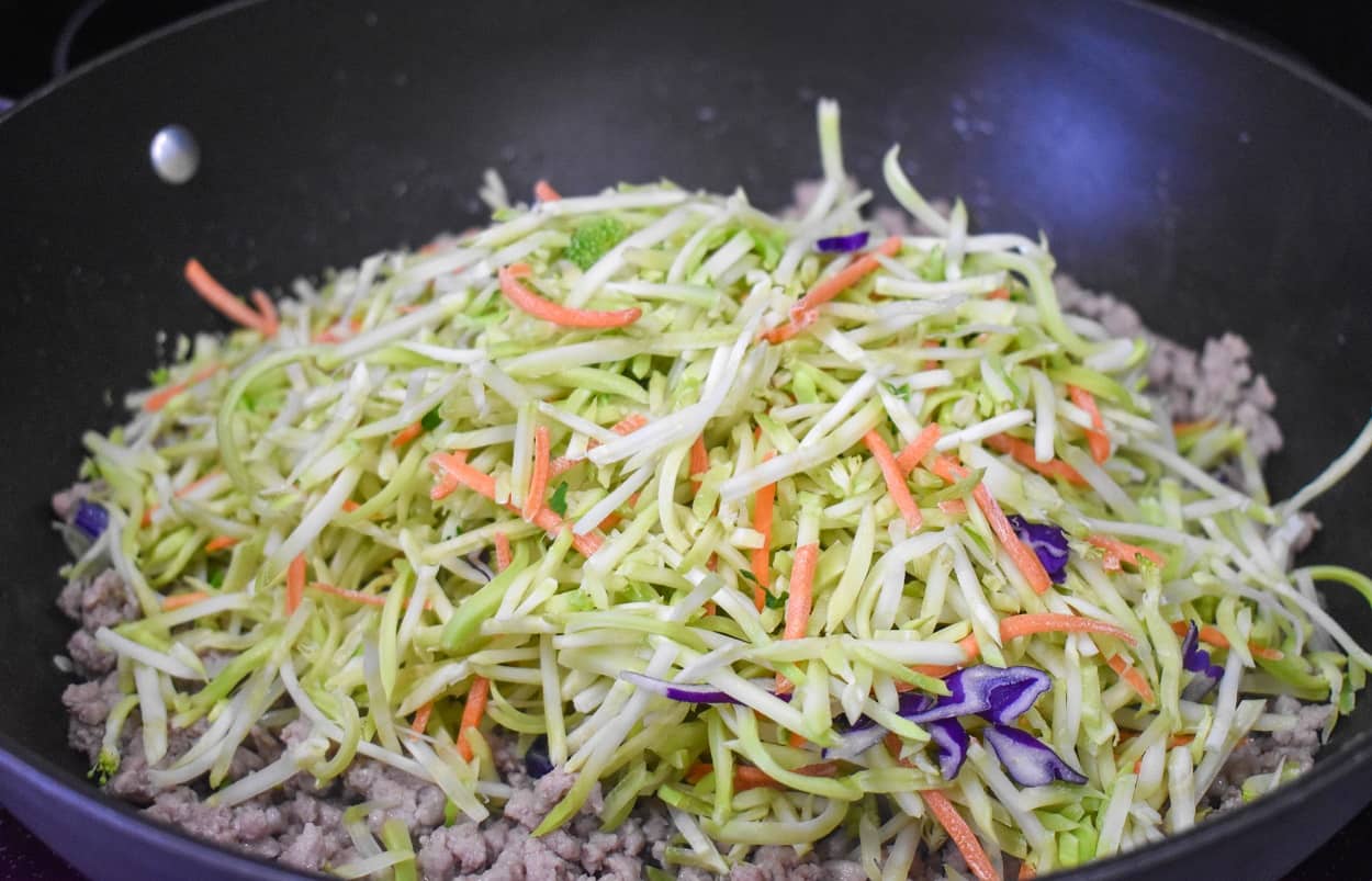 The vegetables on top of the browned ground pork in a large, black skillet.