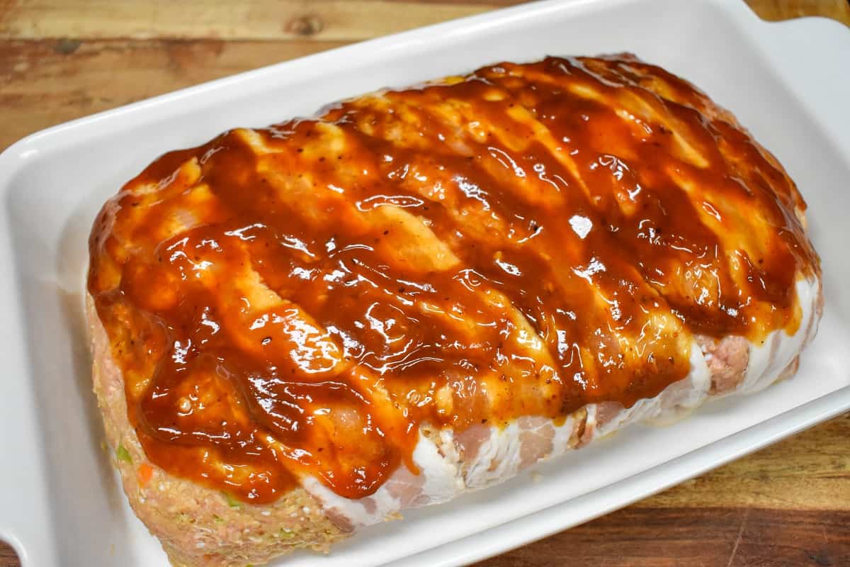 An image of the loaf with the ketchup and steak sauce glaze before baking in a white casserole dish.