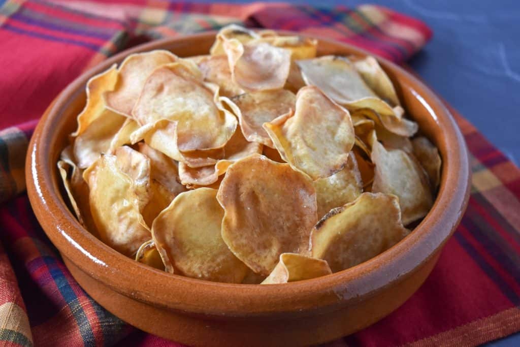 Malanga chips in a terracotta bowl on a red, plaid linen.