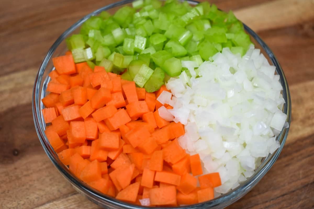 Diced onions, carrots and celery arranged in a glass bowl.