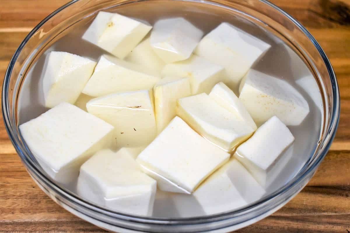 Peeled, cubed malanga covered with water in a glass bowl.