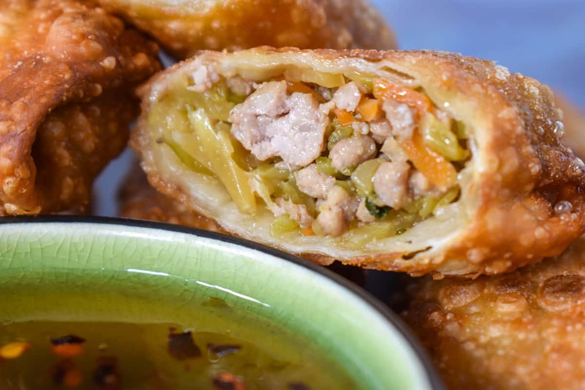 A close up image of the filling of the egg roll that was cut in half, with a small bowl with duck sauce right in front of it.