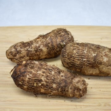 An image of three unpeeled malangas on a wood cutting board.