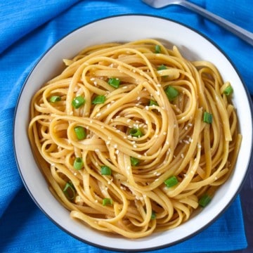 An image of the sesame noodles served in a white bowl with a black rim set on a blue linen.