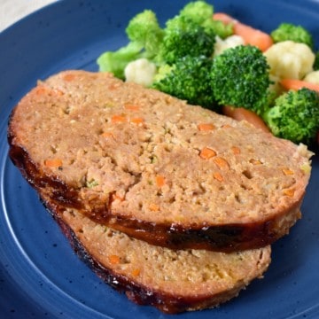 An image of two slices of meatloaf served with a side of vegetables on a blue plate.