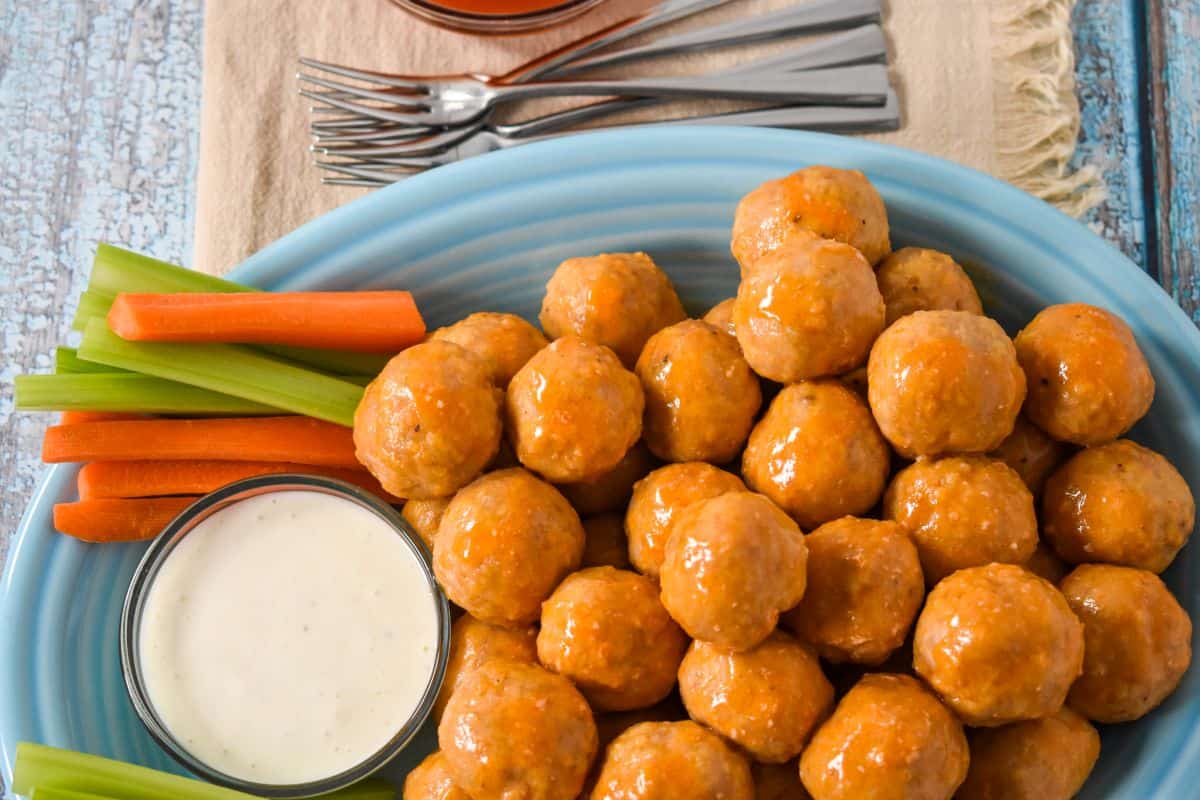 Close-up of buffalo chicken meatballs on a blue platter with ranch, celery, and carrots.