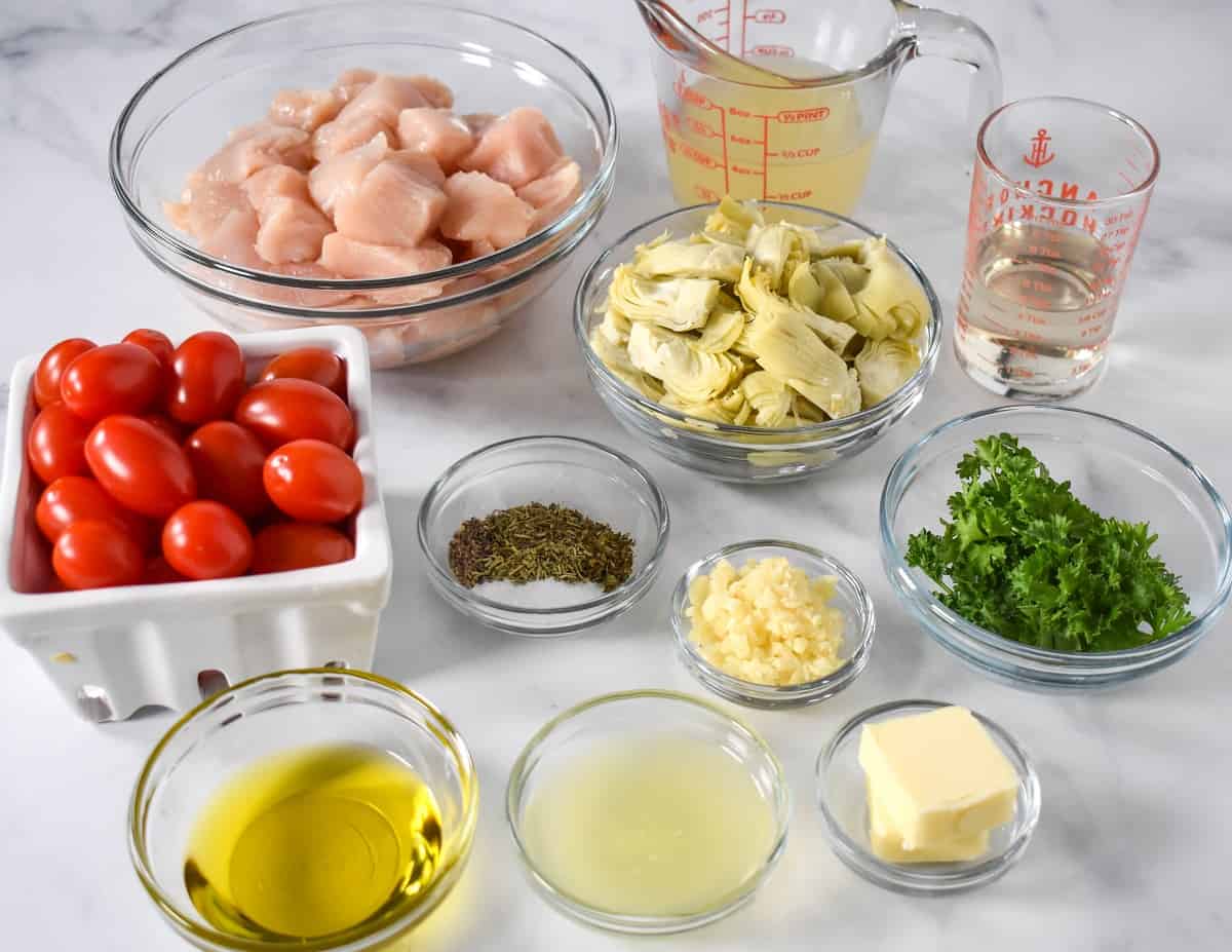 The prepped ingredients for the dish separated in glass bowls and arranged on a white table.