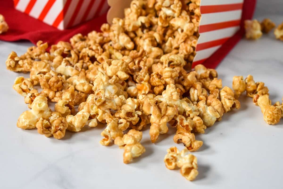 Caramel popcorn spilled on a white table from a small, red and white striped container.