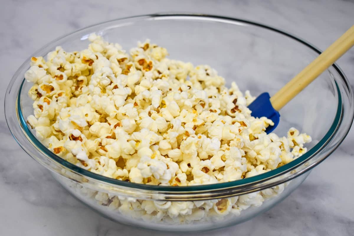 Popcorn in a large, glass bowl with a blue silicone spatula in the bowl to the right.