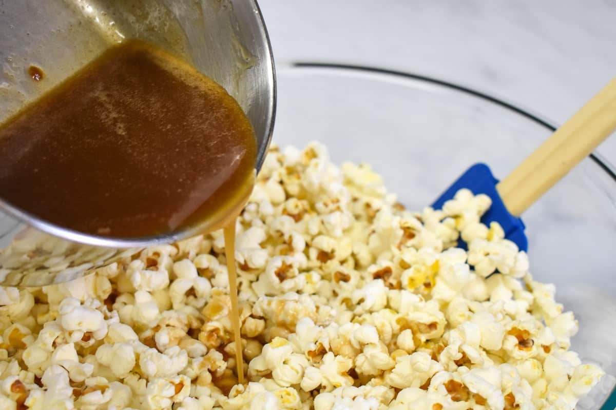 An image of pouring caramel sauce from the saucepan into the large, glass bowl with the popcorn in it.