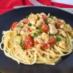 The artichoke chicken served on a bed of linguine noodles on a black plate set on a red linen.