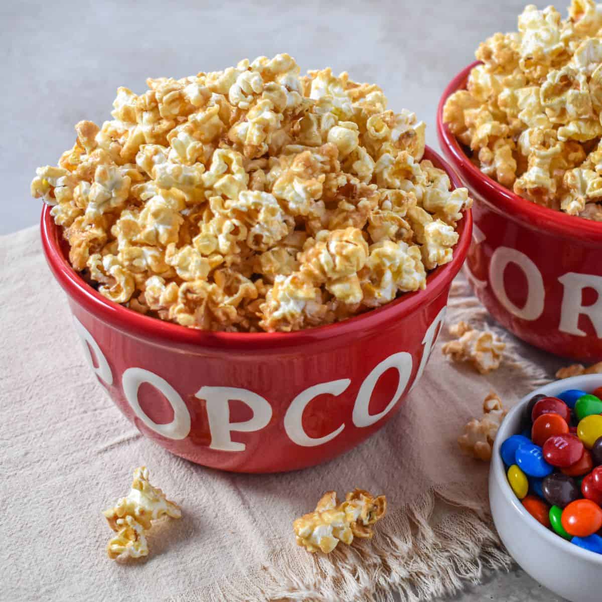 Sweet and salty caramel popcorn in a red bowl with colorful candy nearby.
