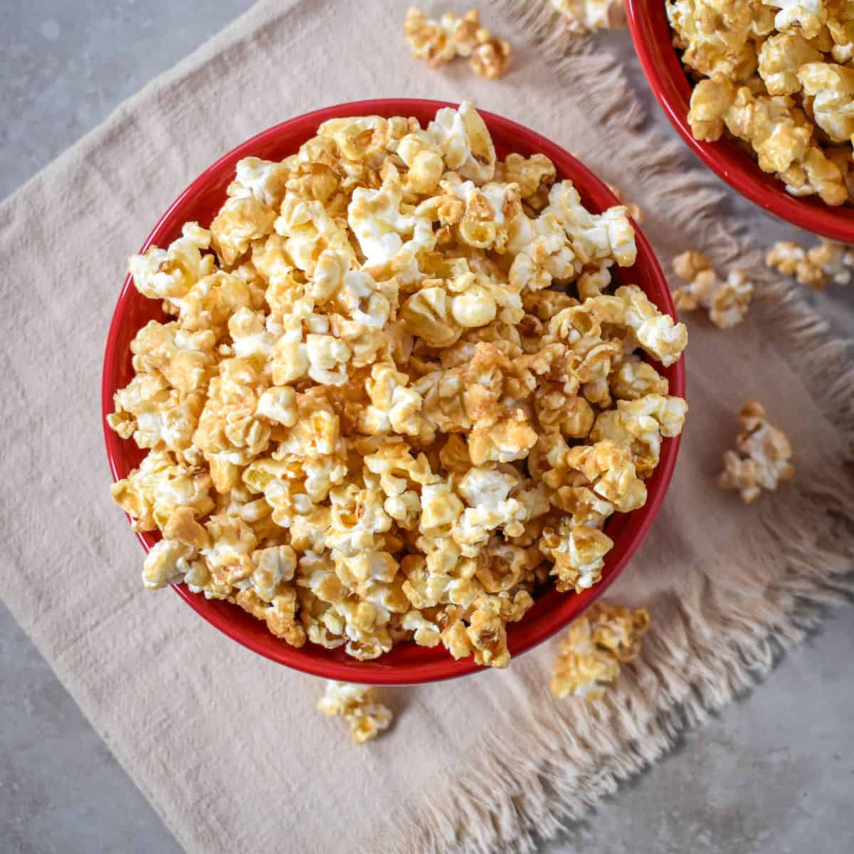 Close-up overhead view of caramel-coated popcorn in a red bowl with pieces scattered around it.
