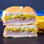 An image of the sandwich one half stacked on the other half with plantain chips on the right side and displayed on a black cutting board on a blue table.