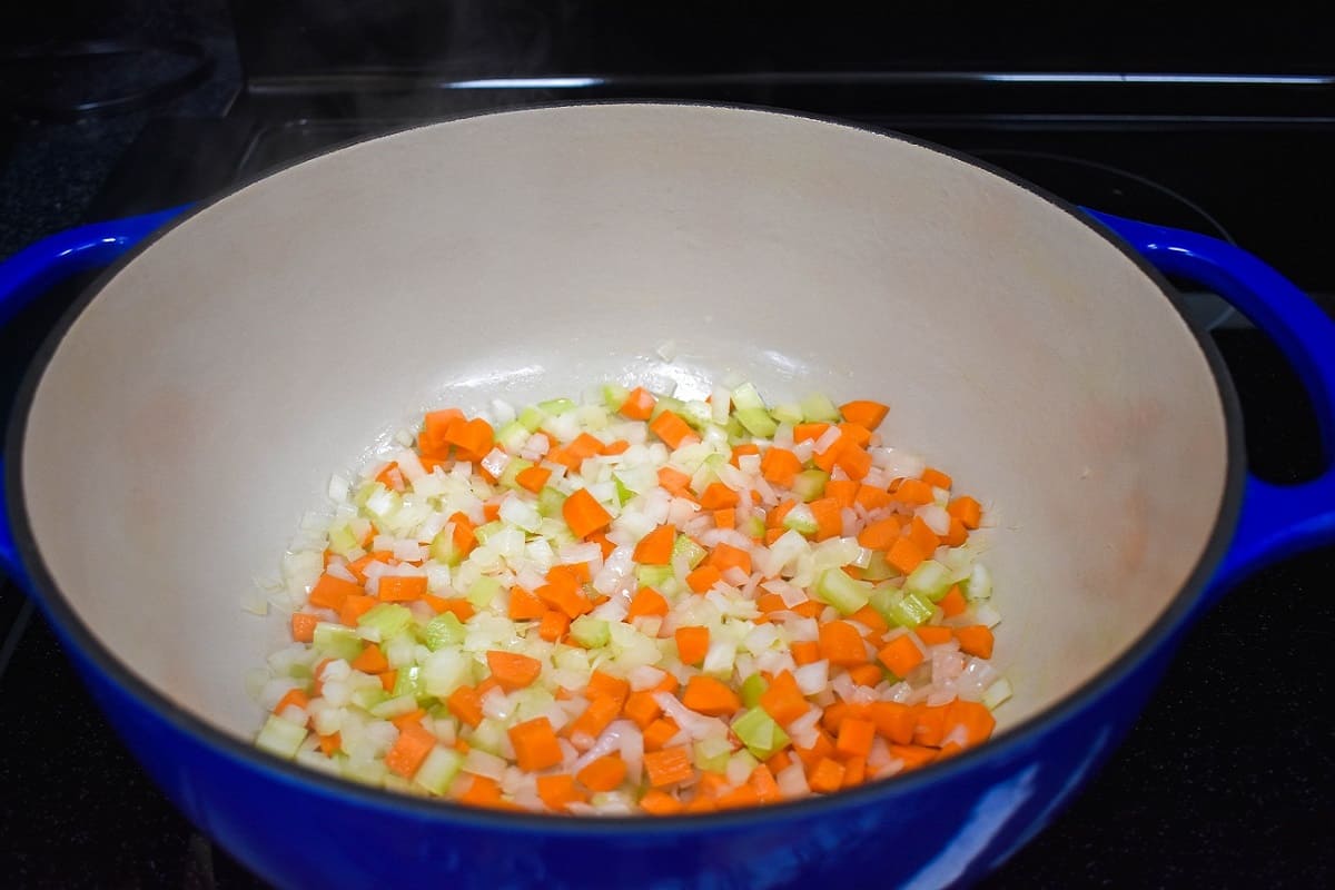Diced onions, carrots, and celery sautéing in a large, blue and white pot.