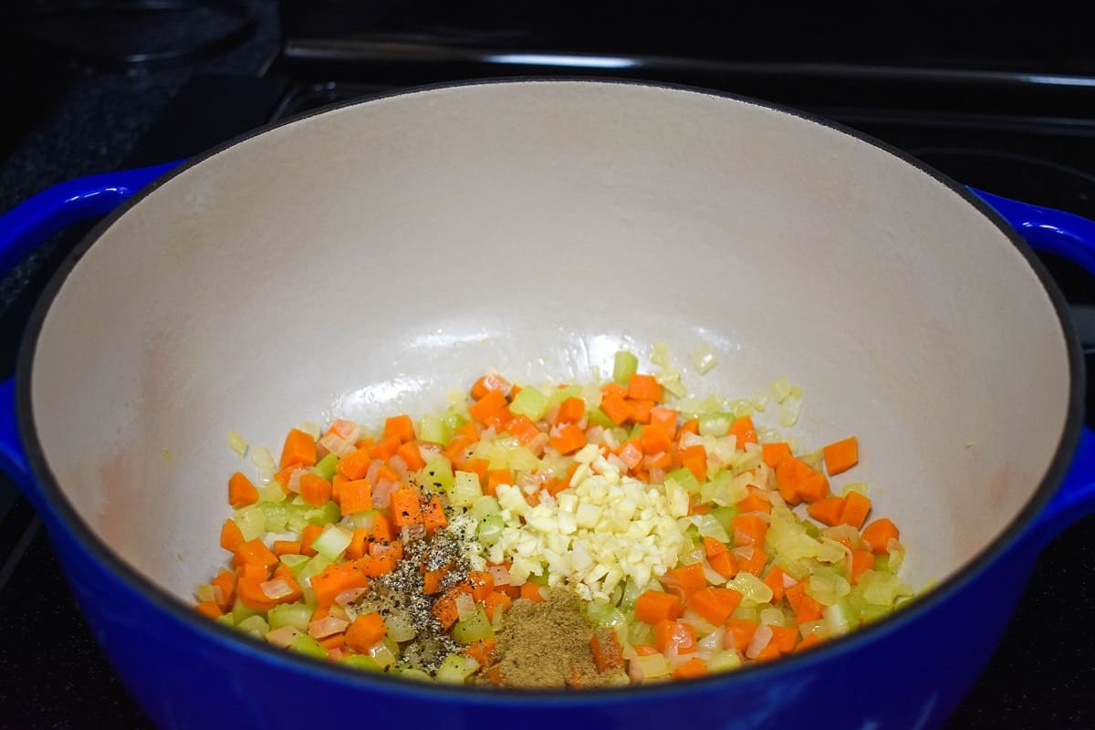 Minced garlic and spices added to the vegetables cooking in a large pot.