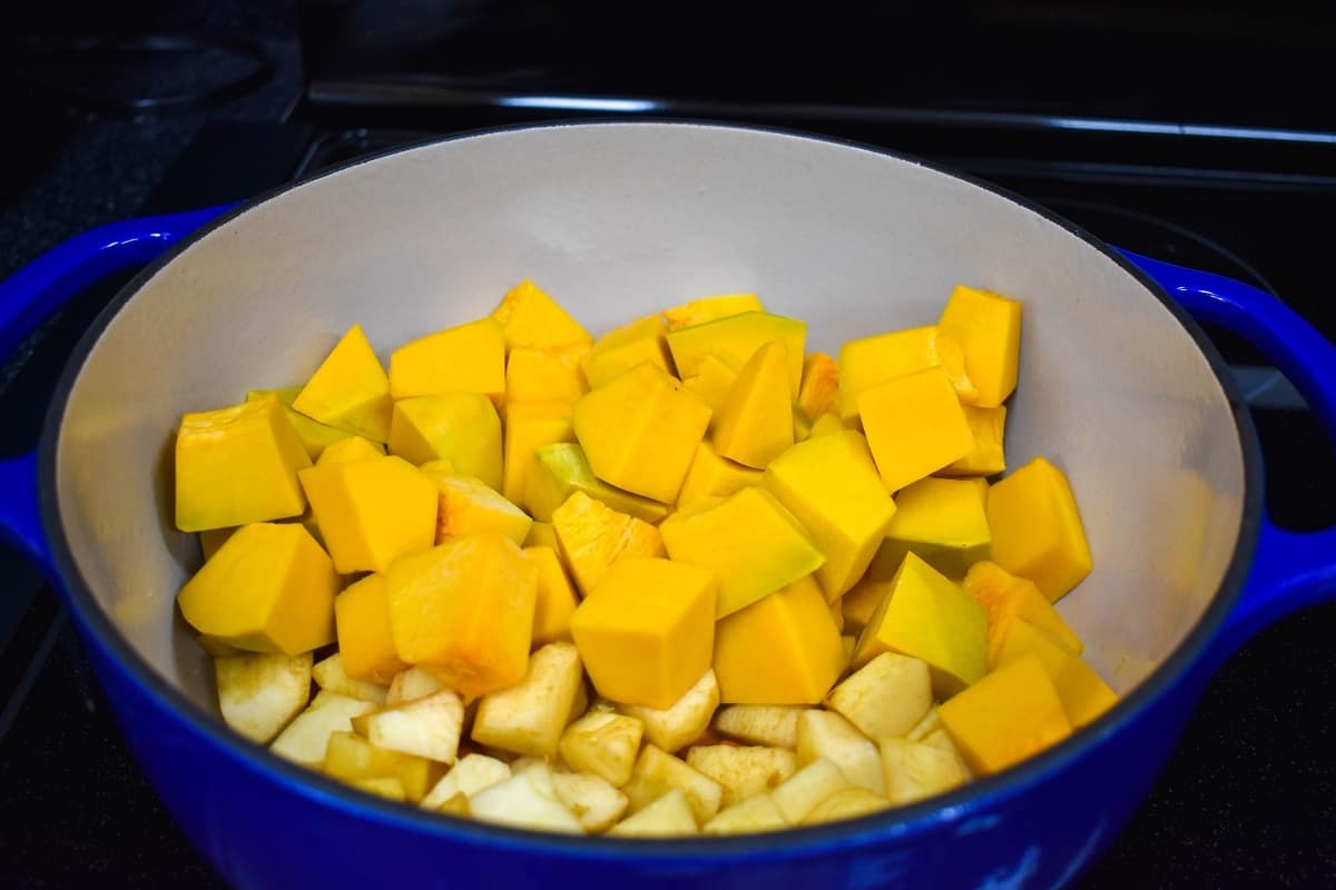 Cut pumpkin and apples in a large blue and white pot.