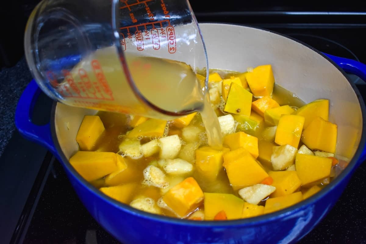 Chicken broth being added to the pumpkin, apples, and other ingredients in the pot.