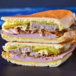 An image of the sandwich one half stacked on the other half with plantain chips on the right side and displayed on a black cutting board on a blue table.