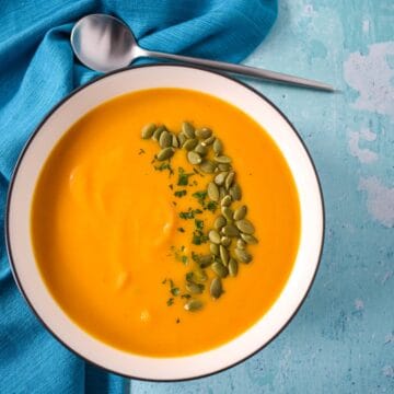 The pumpkin apple soup served in a white bowl and set on a blue table with a blue linen and spoon.