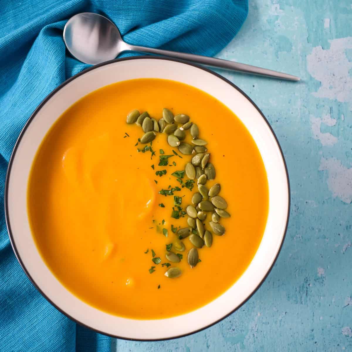 The pumpkin apple soup served in a white bowl and set on a blue table with a blue linen and spoon.