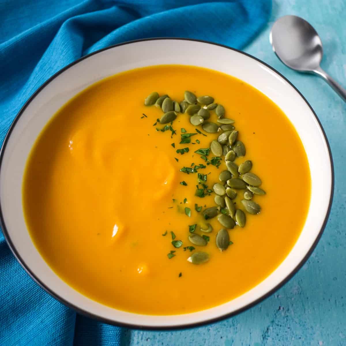 A close up image of the soup served in a white bowl with black rim set on an aqua table with an aqua linen.