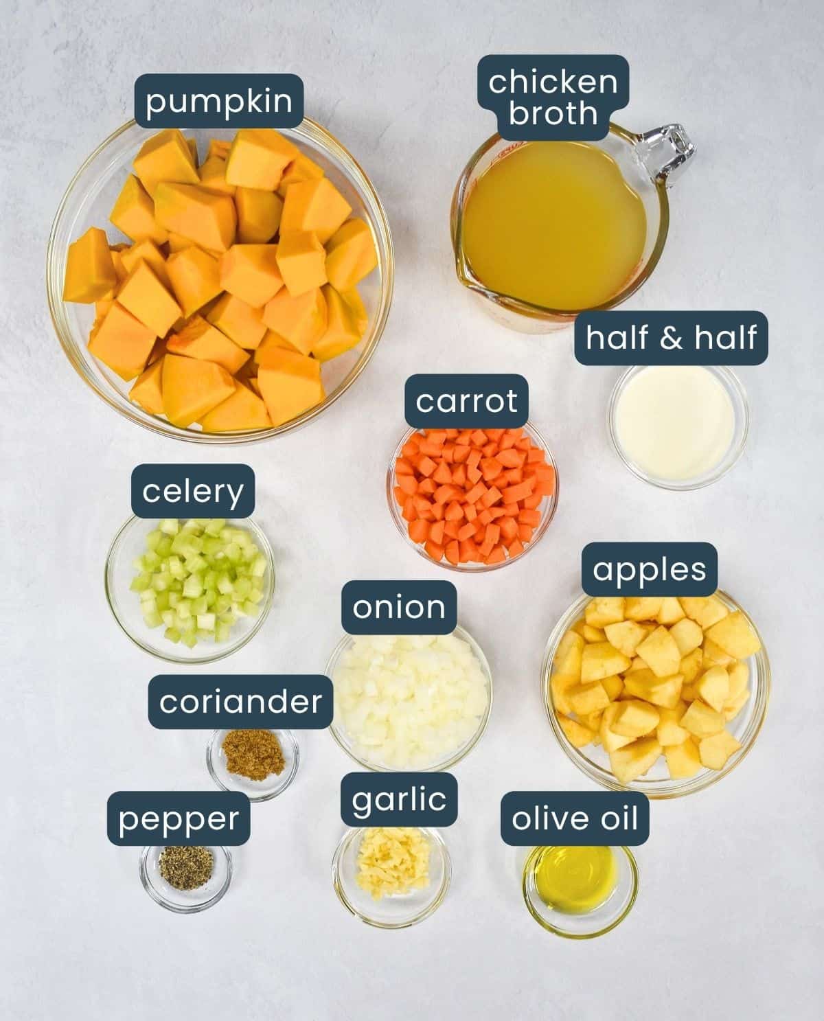 The ingredients for the soup, prepped and arranged in glass bowls on a white table, with each one labeled.