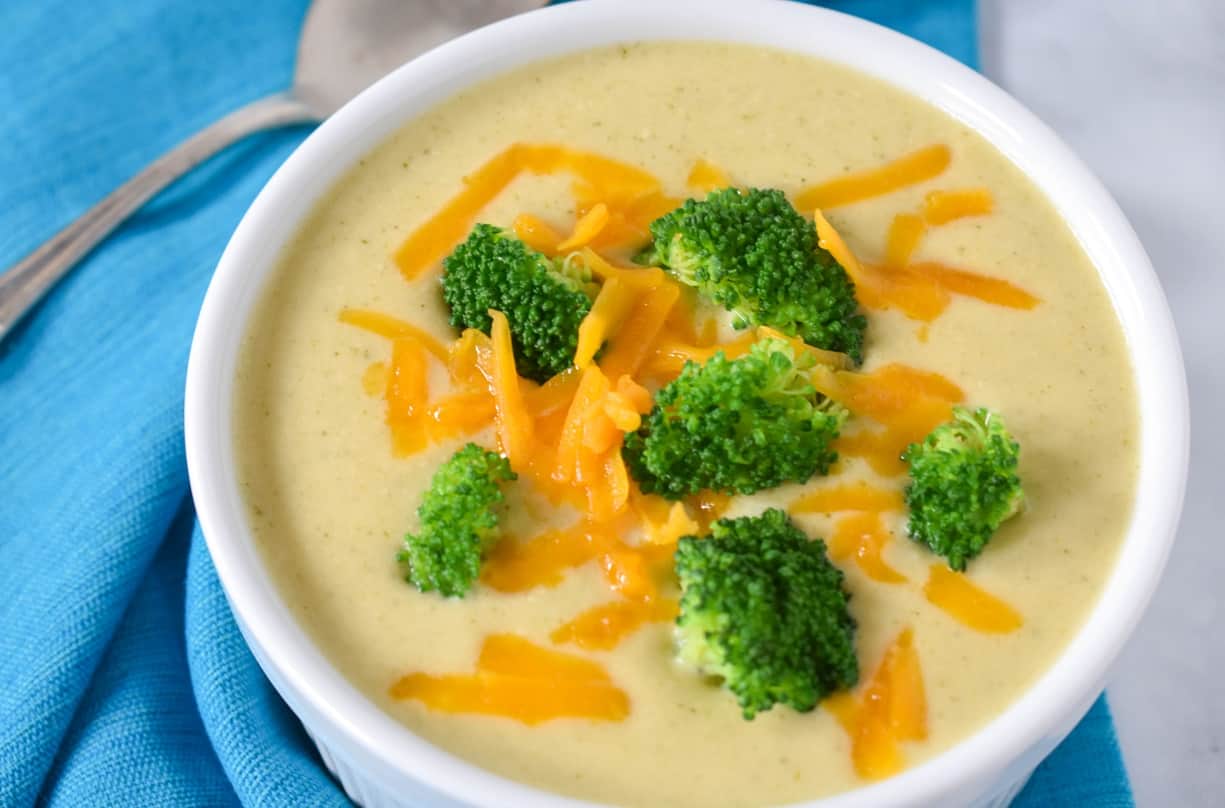 A close up image of the soup garnished with broccoli florets and shredded cheese.