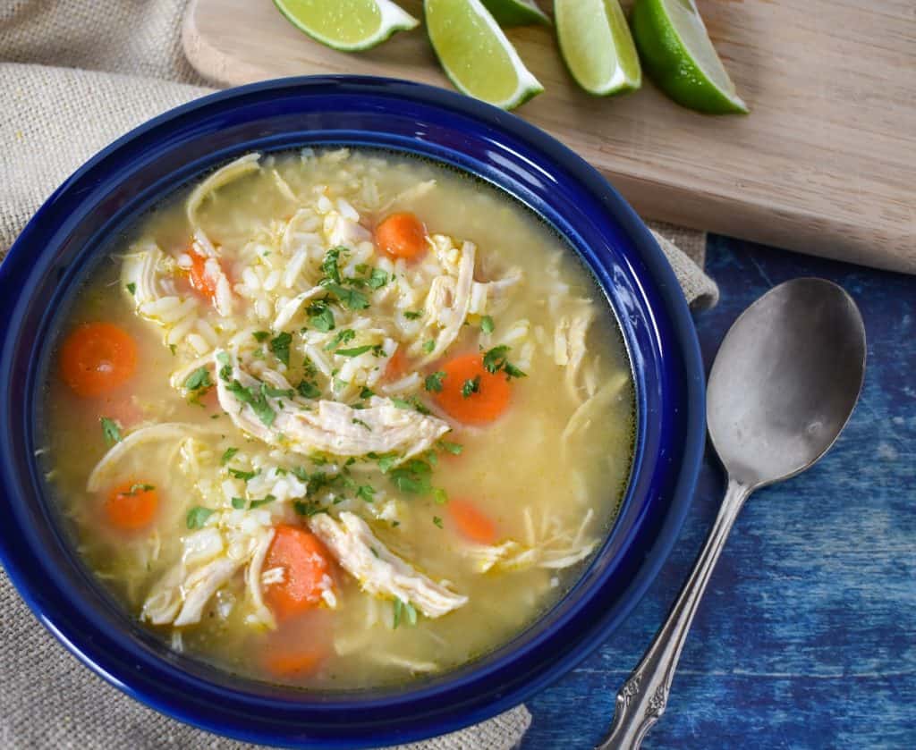 The finished soup served in a blue bowl displayed with lime wedges, a spoon, a beige linen all set on a blue table.
