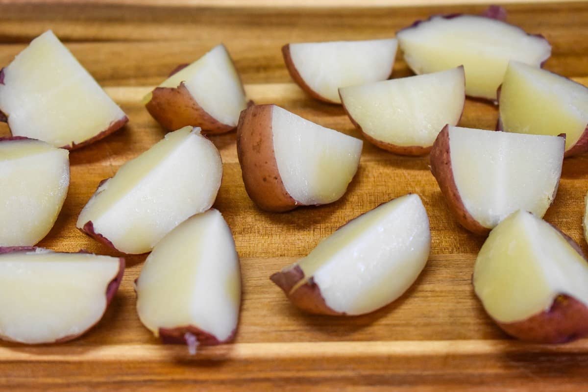 Cooked quartered red potatoes on a wood cutting board.