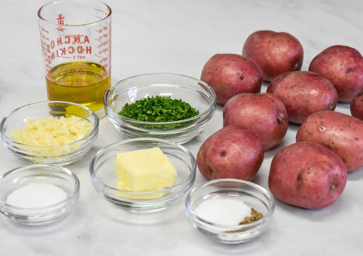 The ingredients for the potatoes prepped and separated into glass bowls with the whole red potatoes to the right side.