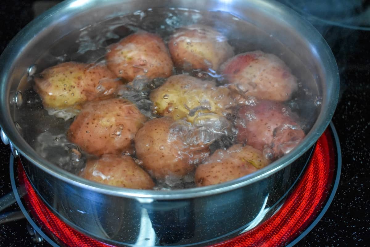 Red potatoes boiling in a pot on a glass top stove.