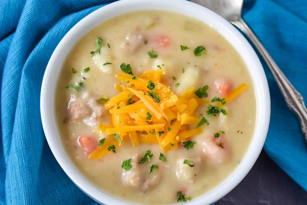 The sausage potato soup served in a white bowl with a blue linen and a spoon on the side..