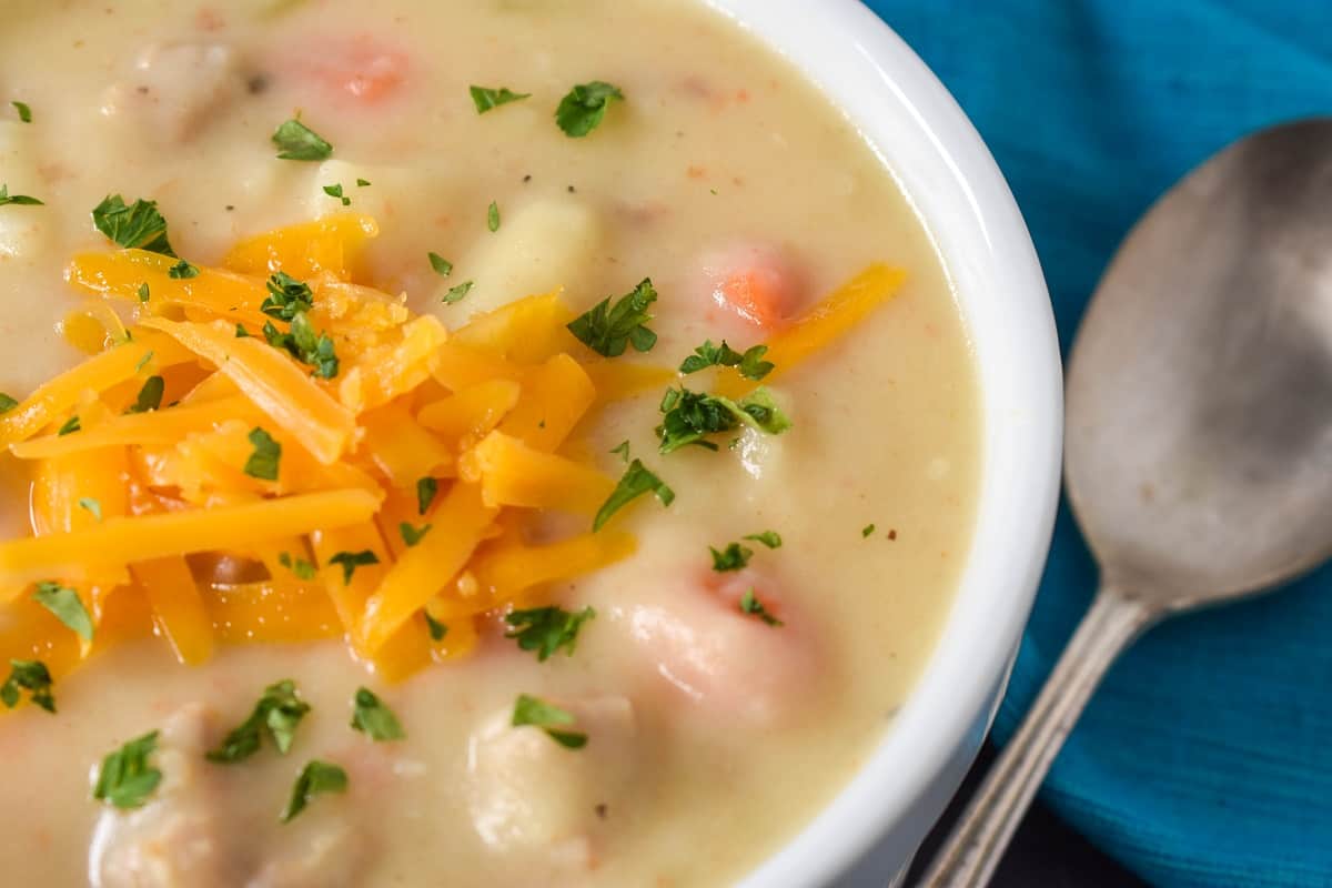 A close up image of the potato sausage soup served in a white bowl with a spoon on the side.