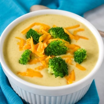 An image of the broccoli cauliflower soup served in a white bowl and garnished with broccoli florets and shredded cheddar cheese.