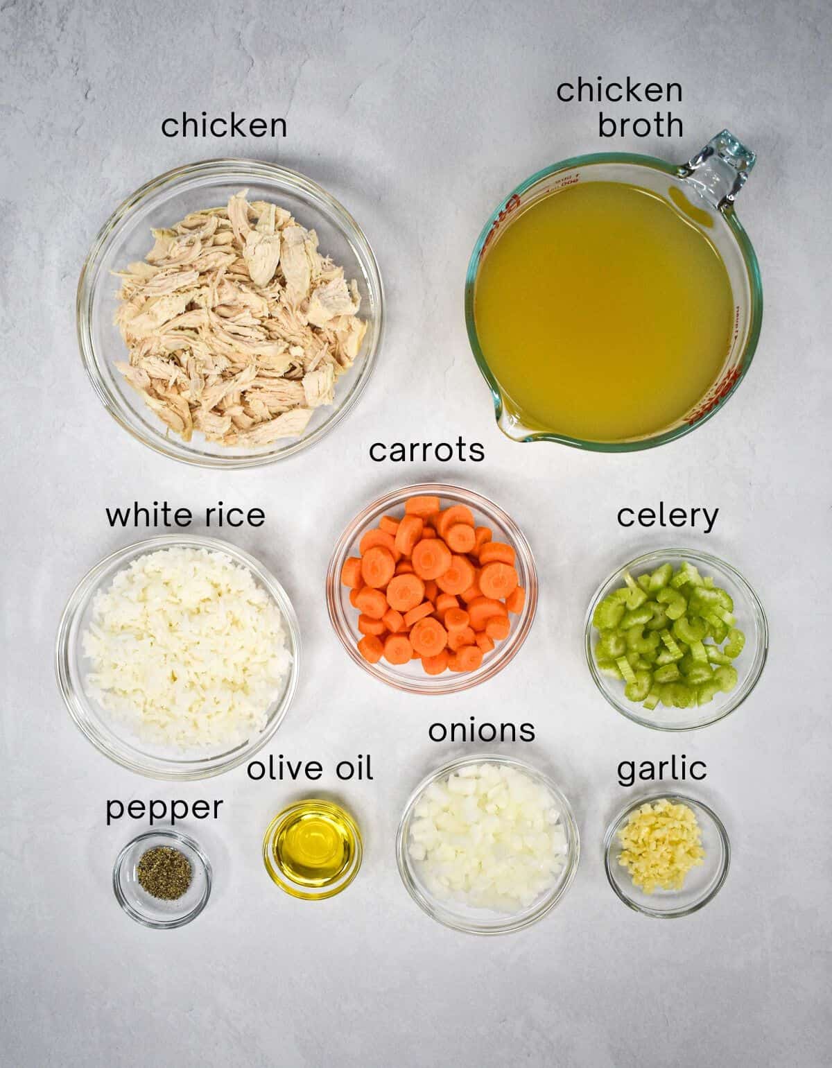 The ingredients for the soup prepped and arranged in glass bowls on a white table with each labeled in small black letters.