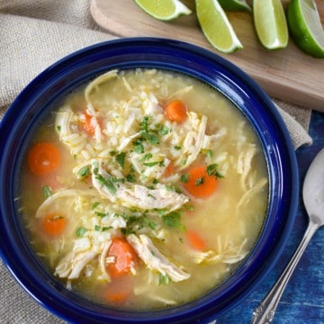 The finished soup served in a blue bowl displayed with lime wedges, a spoon, a beige linen all set on a blue table.