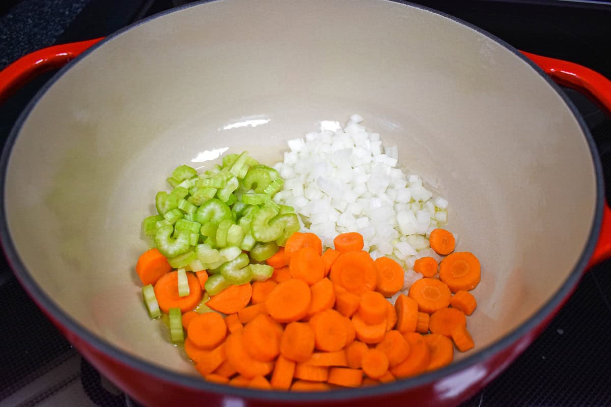 Chopped celery, onions, and carrots in a large red pot before cooking.