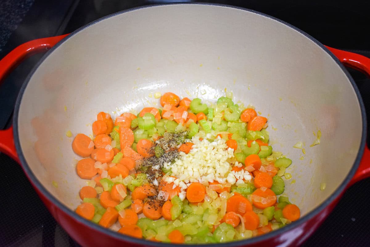 Sautéed vegetables with minced garlic and seasoning added to the pot.