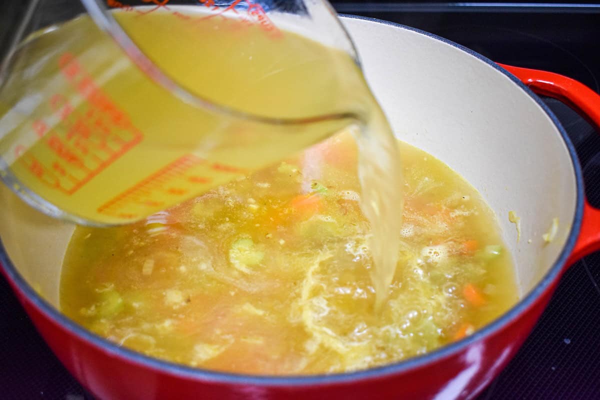 Chicken broth being poured into the pot with sautéed vegetables.