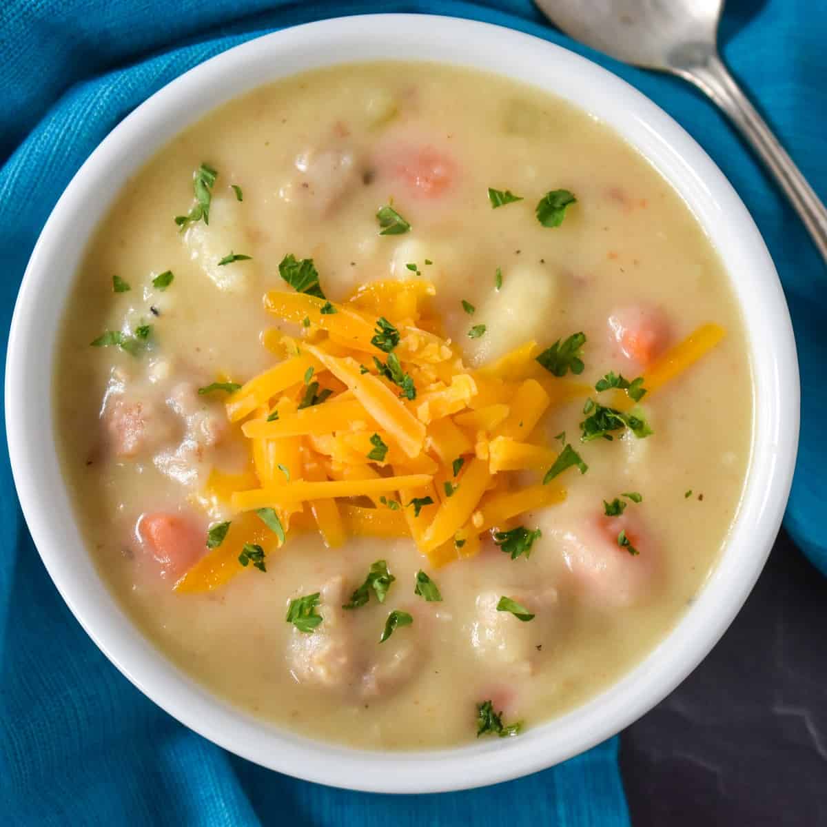 The sausage potato soup served in a white bowl with a blue linen and a spoon on the side.