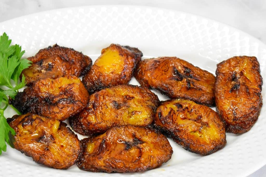 The fried plantains arranged on a white plate with parsley as a garnish on the left side.